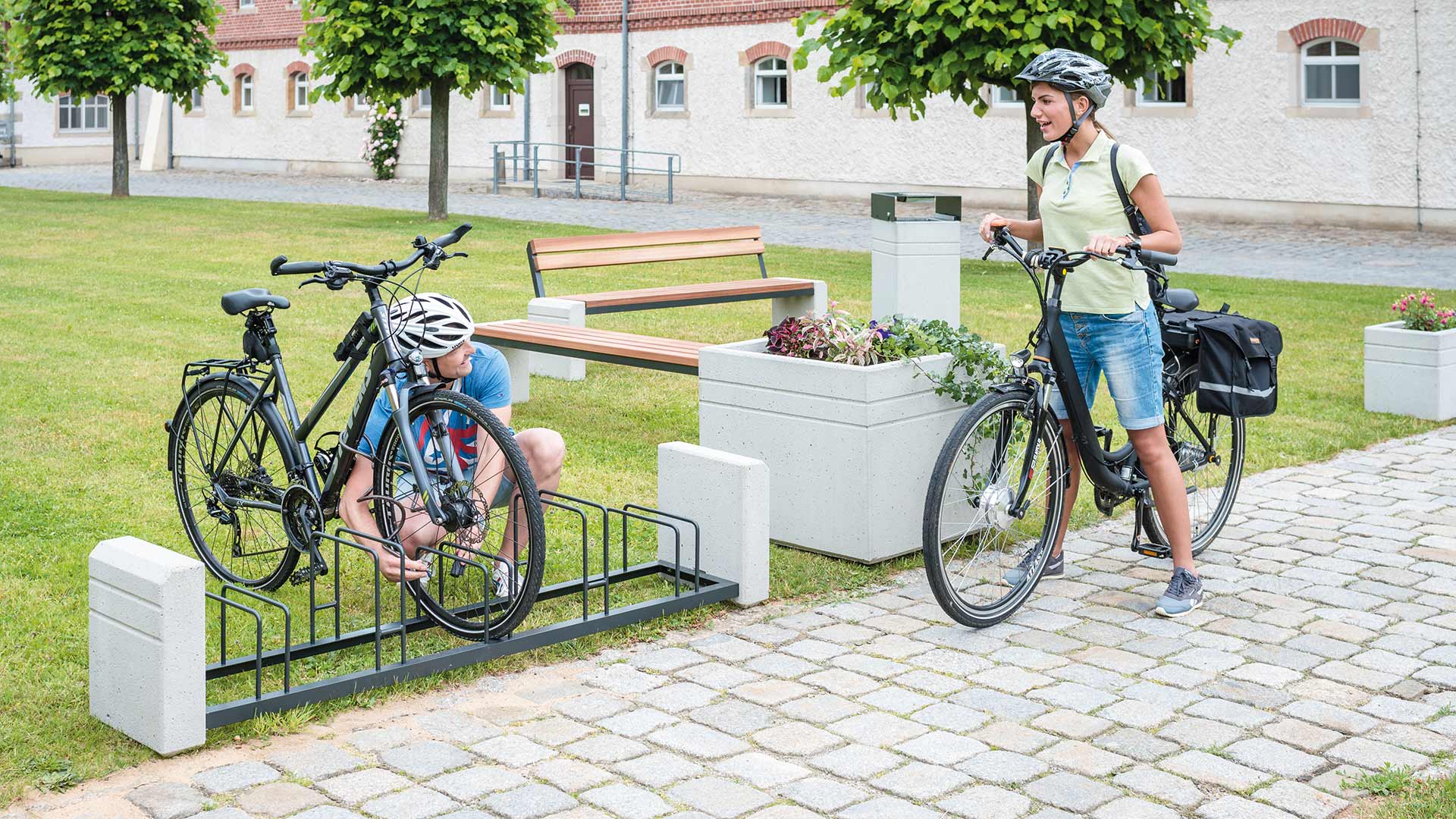 Zwei Personen mit Fahrrädern, einer befestigt sein Rad an einem Fahrradständer