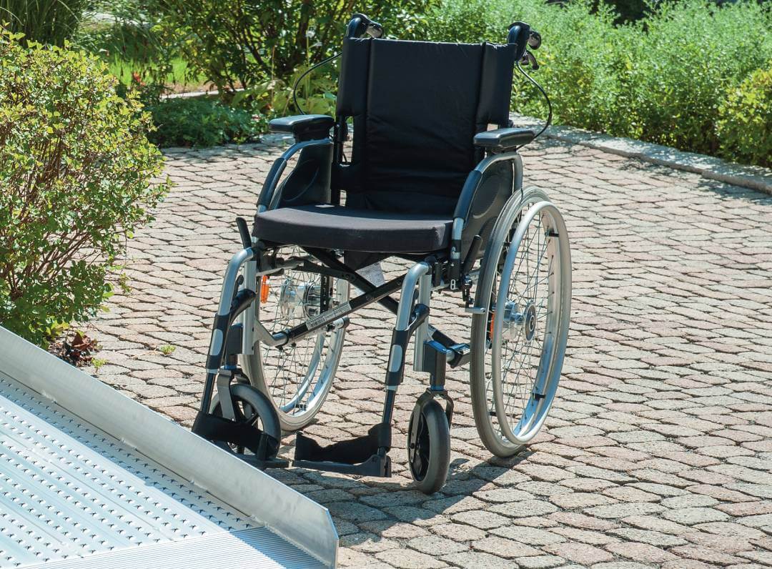 Rollstuhl auf einem Pflasterweg hinter einer Rampe aus Metall