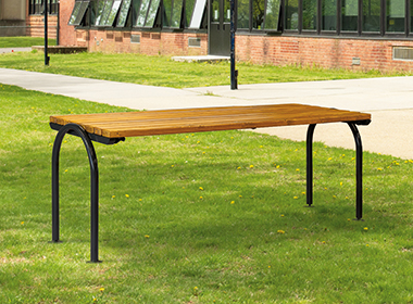 Moderner Tisch SAN REMO mit Holzplatte und schwarzen Metallbeinen steht auf einer Rasenfläche vor einem Backsteingebäude.