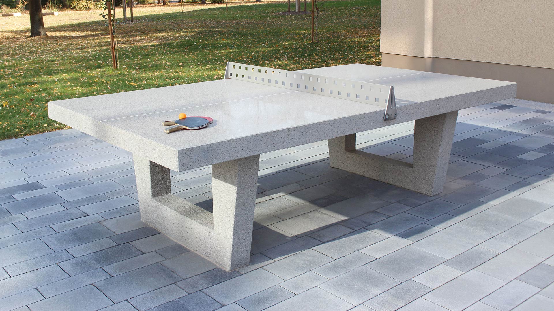 Outdoor Tischtennisplatte aus Beton mit Schlägern und Ball auf Pflastersteinen