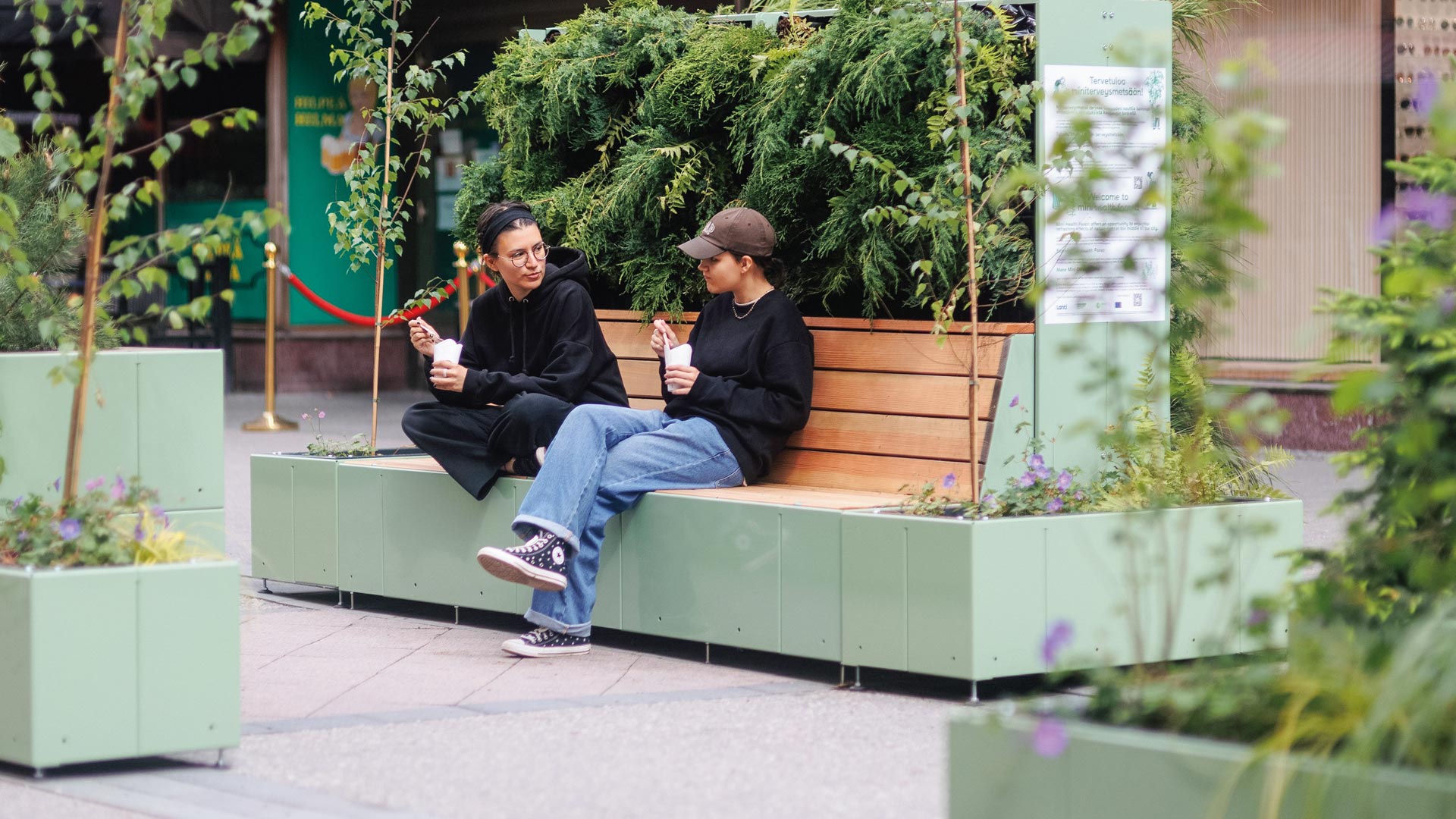 Zwei Personen sitzen auf einer Sitzinsel TASKU mit Begrünung