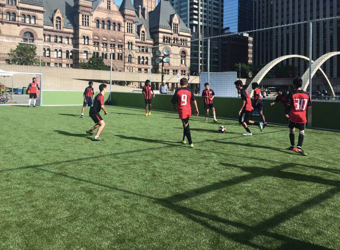 Kinder spielen Fußball auf einem umzäunten Sportplatz in einer Stadt