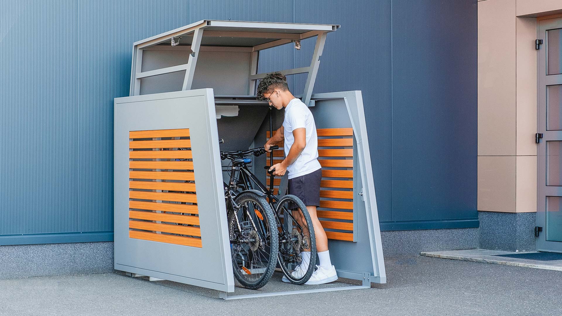 Moderne Fahrradbox mit Holzlamellen in grau - Mann verstaut sein Fahrrad