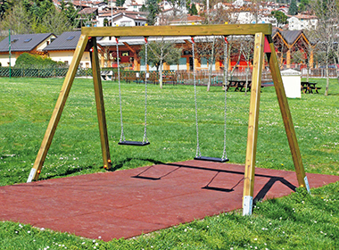 Doppelschaukel mit Holzgestell und zwei schwarzen Sitzflächen auf rotem Bodenbelag im Freien.
