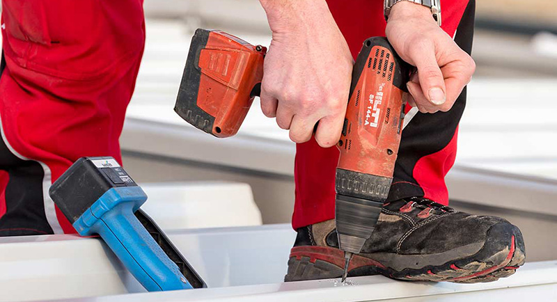 Person in roter Arbeitskleidung bohrt mit einem Akkuschrauber in die Sohle eines schwarzen Arbeitsschuhs