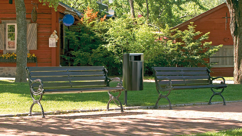 Grüner Abfallbehälter neben einer grünen Bank im Park