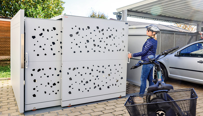 Frau mit Fahrrad öffnet eine moderne, graue Fahrradbox