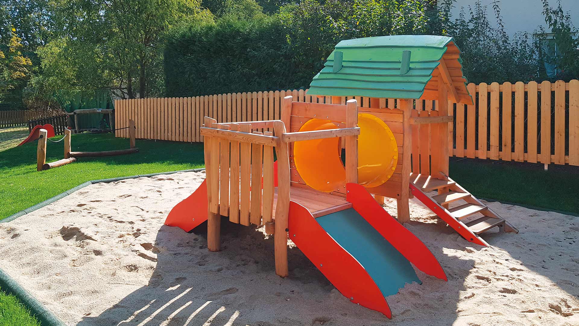 Spielplatzgerät mit Holzgerüst, kleinen Rutschen, Spieltunnel auf einem Sandkasten