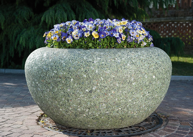 Großer runder Marmor-Pflanzbehälter mit blühenden Stiefmütterchen auf gepflastertem Boden
