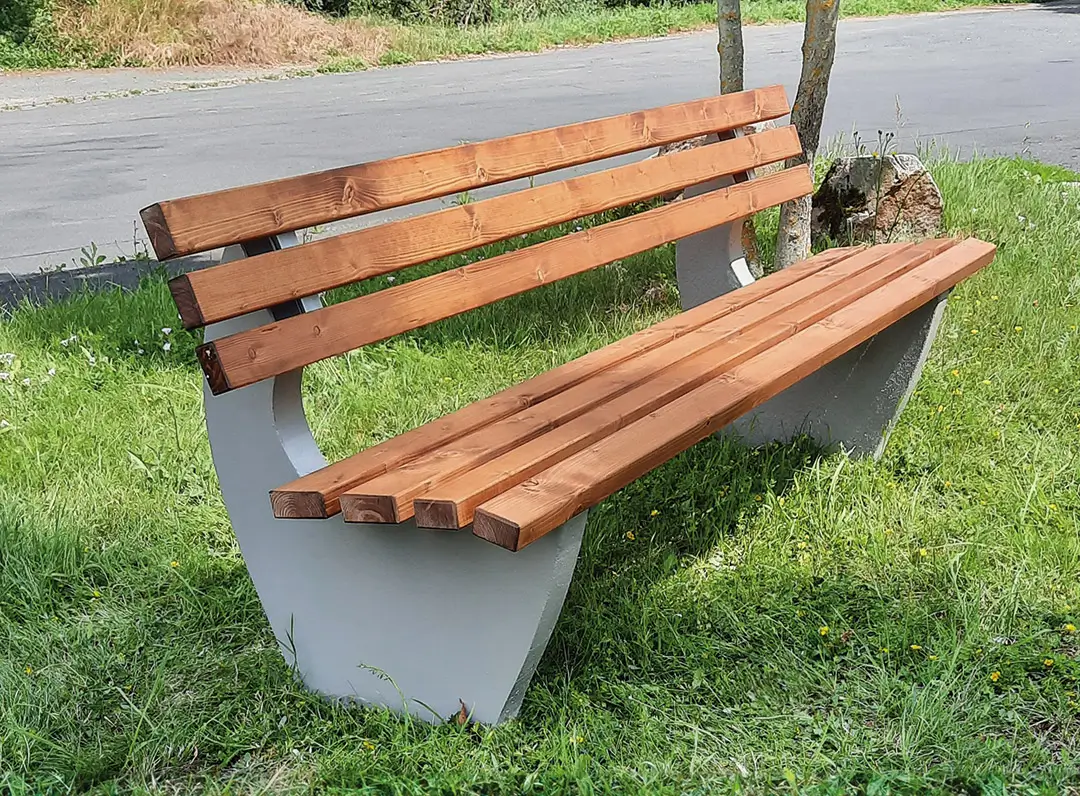 Sitzbank GENOVA mit Holzlatten und grauen Betonfüßen steht auf Gras neben einem Weg.