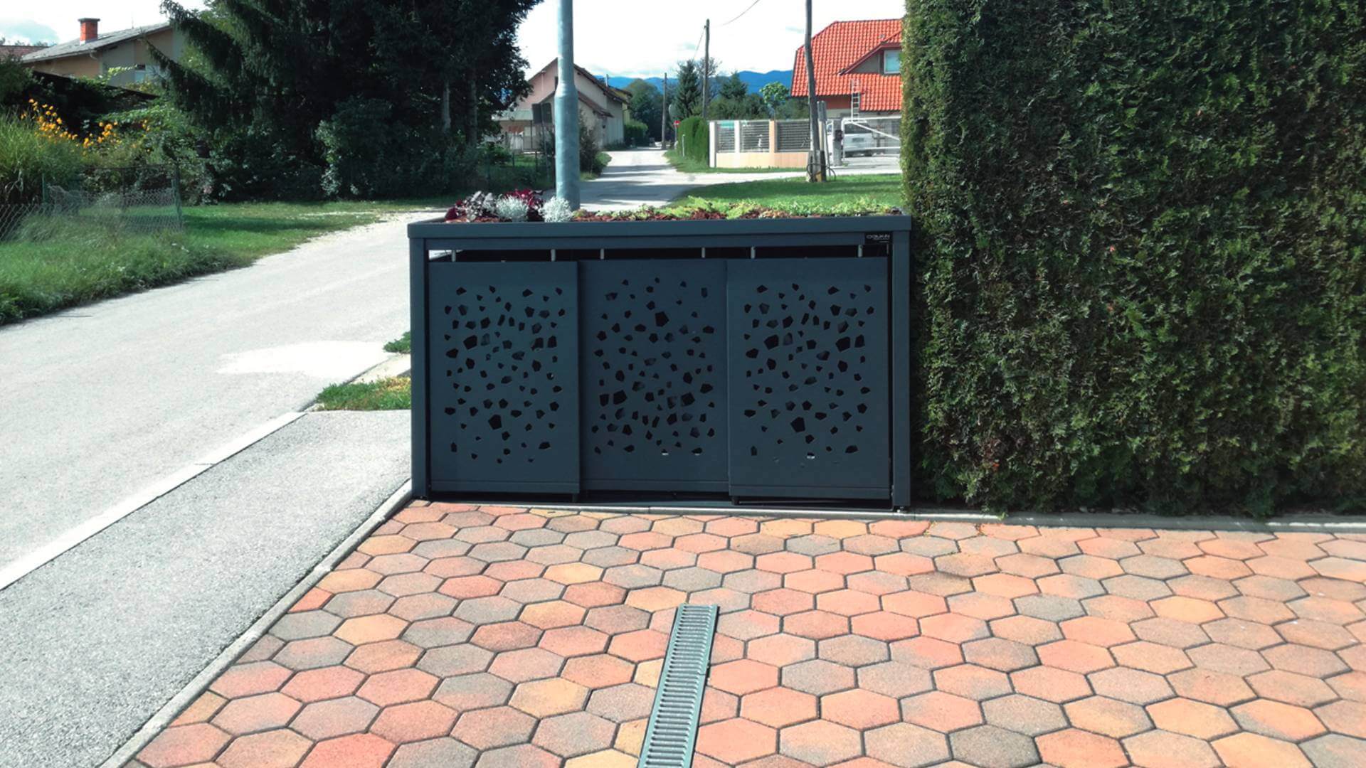 Mülltonnenbox mit Lochoptik vor einer Einfahrt