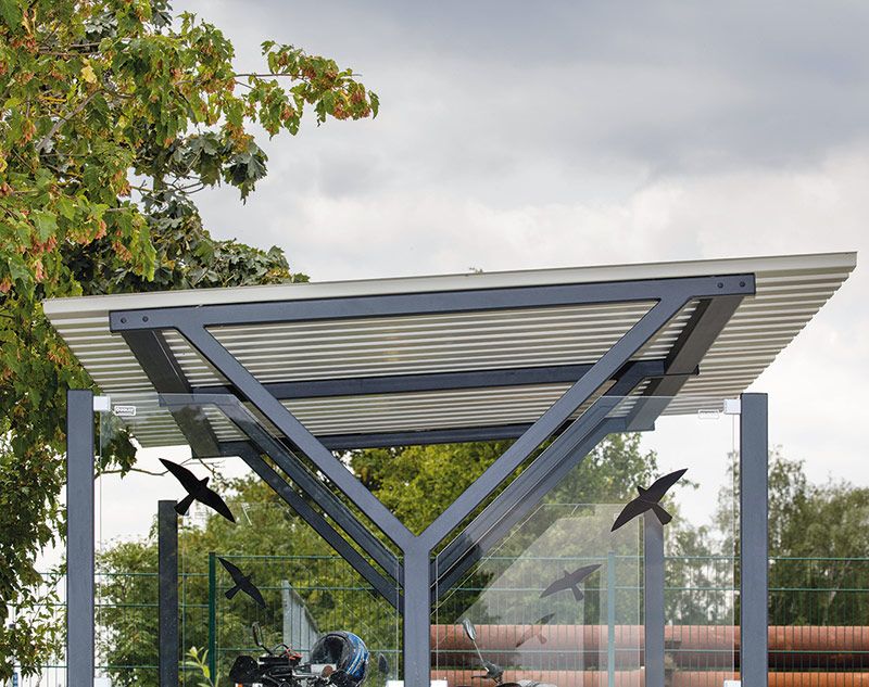 Fahrradüberdachung mit transparentem Dach und Metallrahmen vor bewölktem Himmel