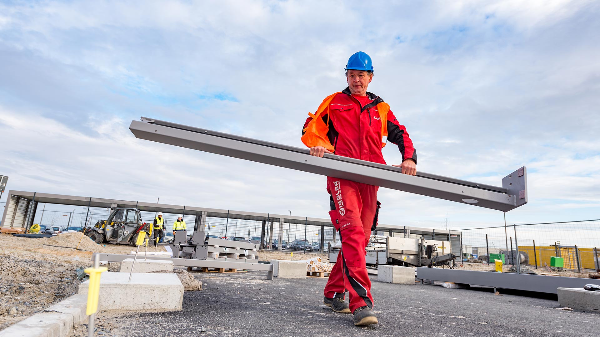 Ein Bauarbeiter von ZIEGLER trägt einen Stahlträger auf einer Baustelle