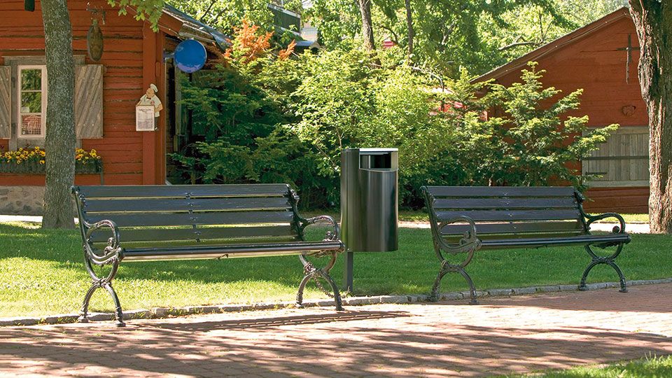 Grüner Abfallbehälter neben einer grünen Bank im Park