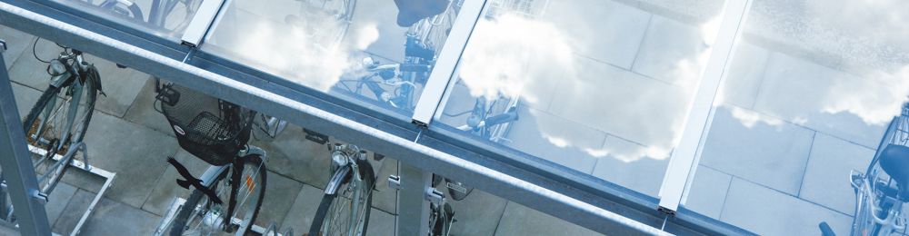 Fahrräder unter einer transparenten Fahrradüberdachung mit Metallrahmen auf gepflastertem Boden